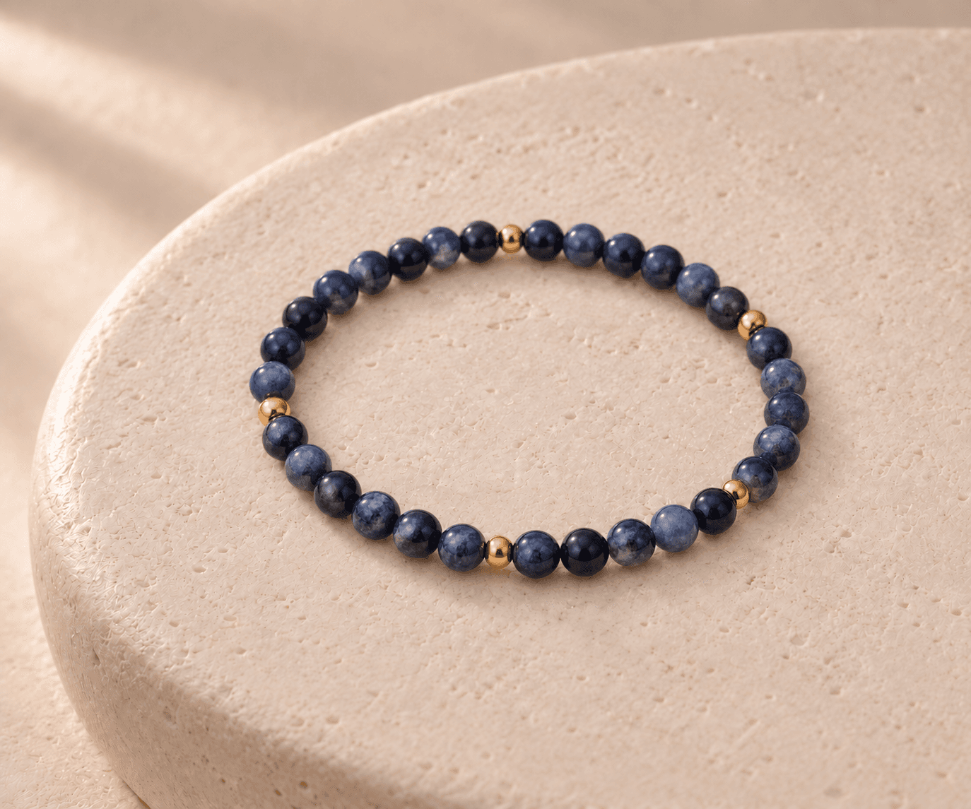 Water bead bracelet in midnight blue with small gold spacers on a rounded cream stone pedestal, without a pendant