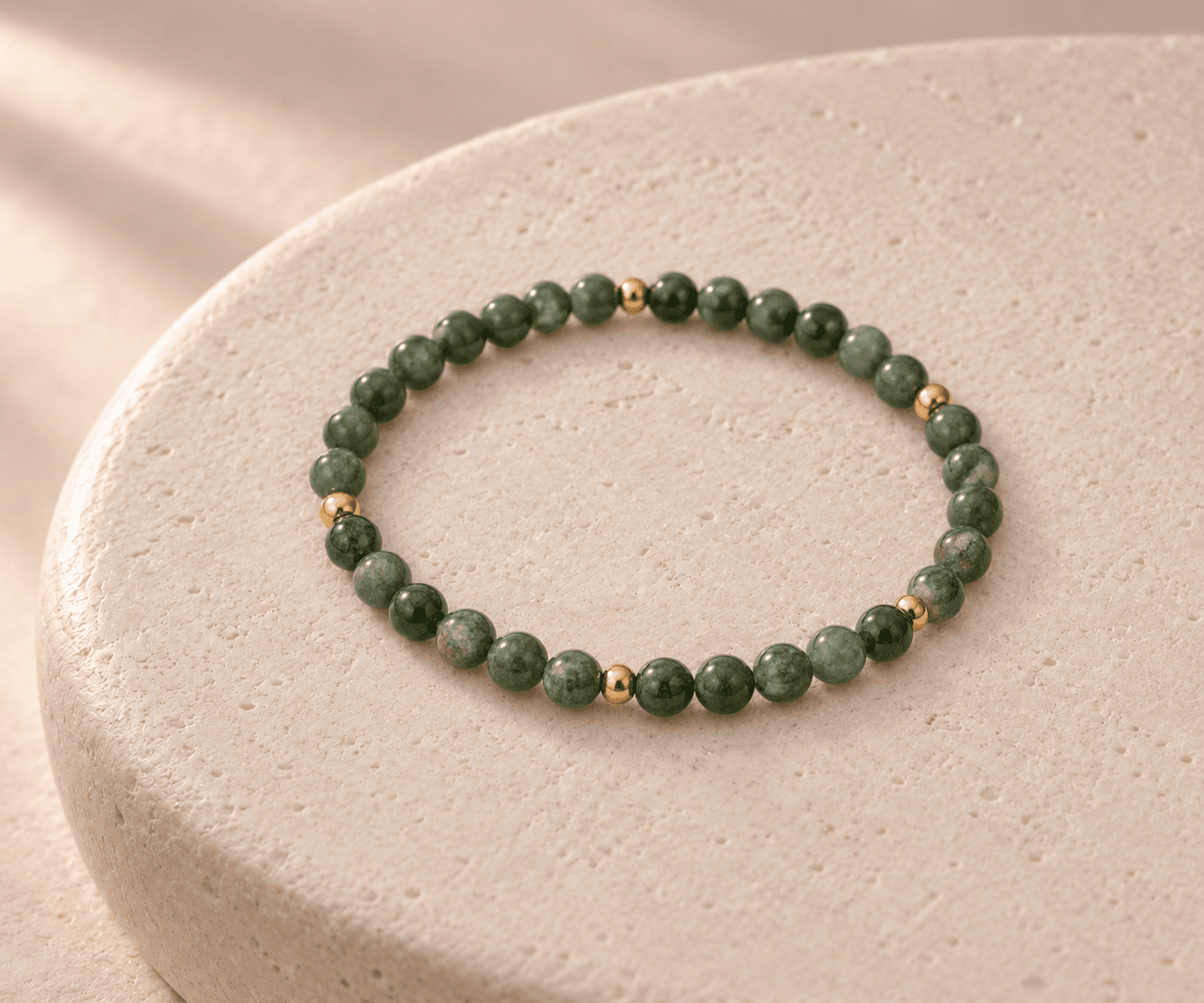 Wood bead bracelet in moss green with small gold spacers on a rounded cream stone pedestal, without a pendant
