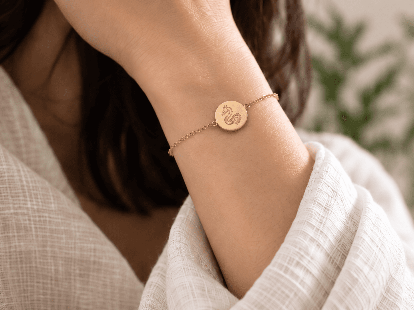 Concept image of a fine gold chain bracelet with a Dragon medallion worn beside an ivory linen cuff