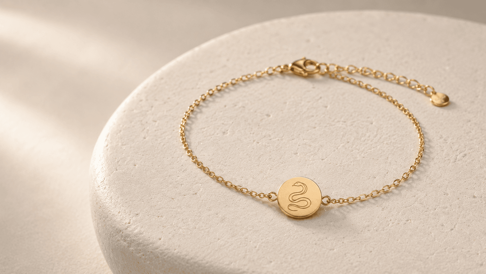 Design concept of a complete gold-tone Snake zodiac chain bracelet with engraved medallion, clasp and extension chain on pale stone